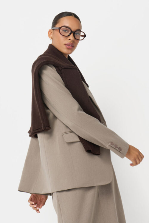 On-model photography of a taupe oversized blazer with a dark brown sweater draped over one shoulder, shown in side profile