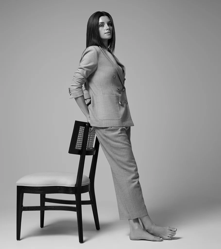 Black and white on-model photography of a grey suit, model leaning against a chair in side profile