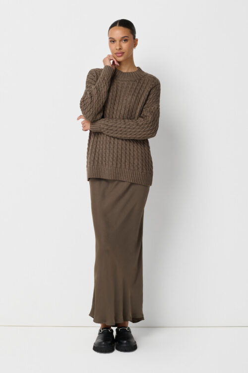 On-model photography of a taupe cable-knit sweater layered over a satin maxi skirt with chunky loafers