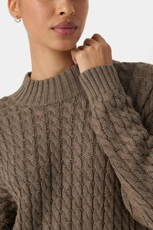 On-model photography close-up of a taupe cable-knit sweater with a ribbed mock neck and cuff detail