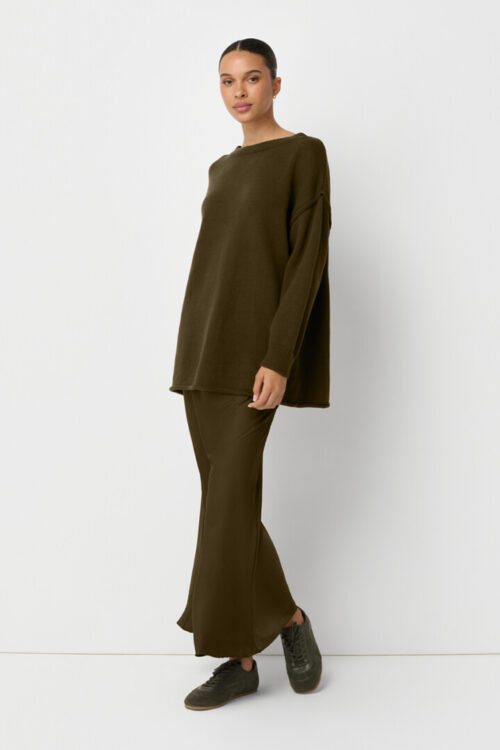 On-model photography of an olive oversized sweater worn over a matching satin maxi skirt with sneakers