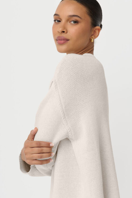 On-model photography of a cream knit tunic worn over a lace-trimmed maxi skirt, shown full length