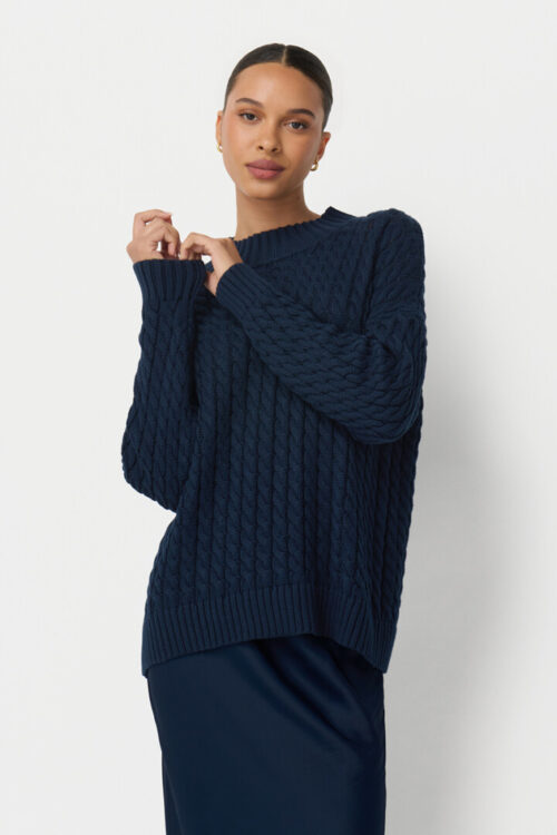 On-model photography of a navy cable-knit sweater worn over a matching navy satin skirt