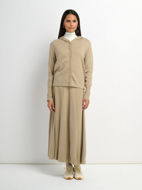 On-model photography of a beige hooded cardigan worn over a matching flared maxi skirt with lace-up sneakers