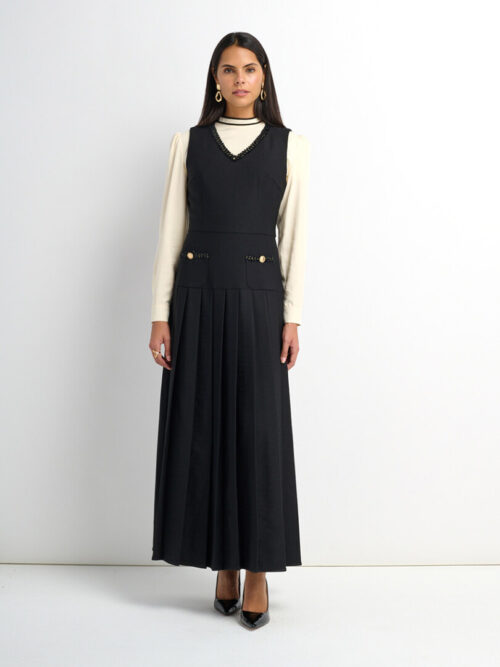 On-model photography of a black sleeveless pinafore maxi dress layered over a cream long-sleeve top