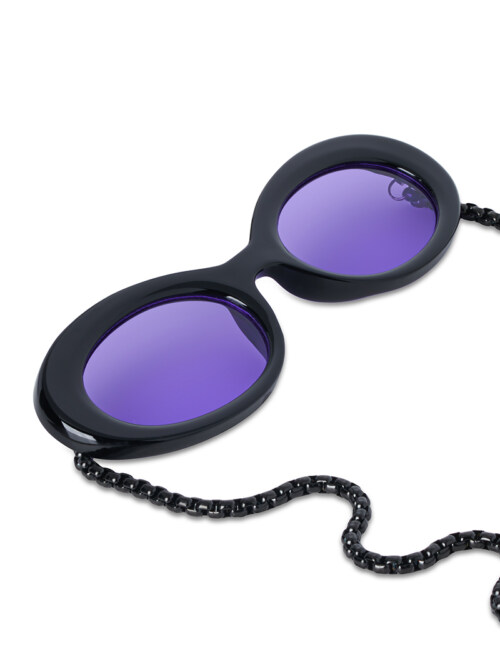 Close-up product photography of black oval sunglasses with violet lenses attached to a beaded chain, angled view