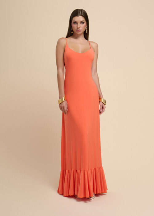 On-model photography of a coral slip maxi dress with thin straps and a ruffled hem, styled with stacked gold bangles