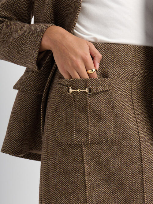 On-model photography close-up of a herringbone tweed skirt pocket with a gold horsebit clasp