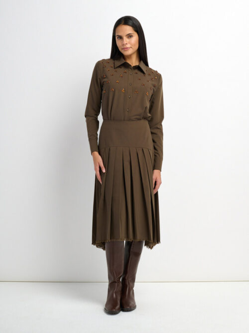 On-model photography of an olive shirt dress with jewel embellishments and a pleated drop-waist skirt, worn with tall boots