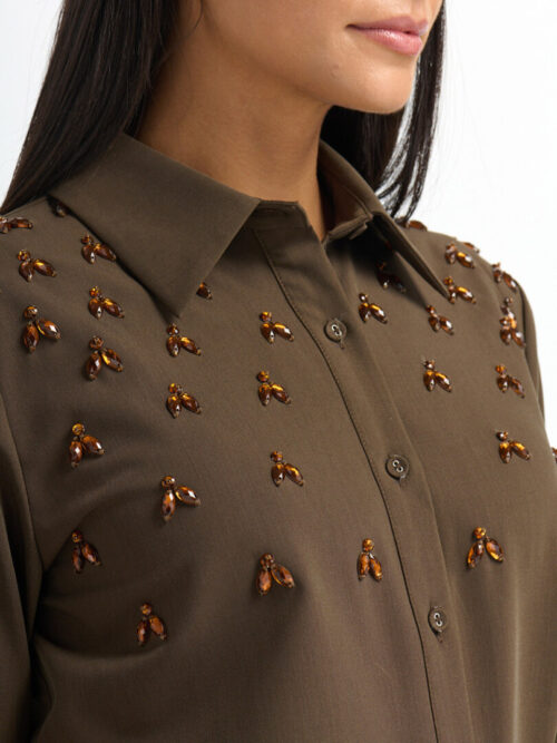 On-model photography close-up of amber jewel embellishments across the collar and front of an olive shirt