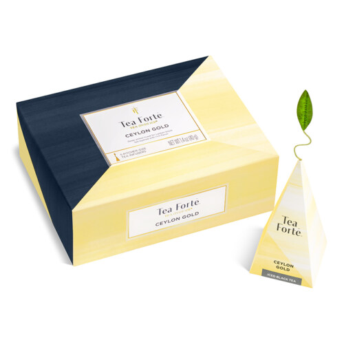 Product photography of a closed yellow and navy tea box next to a pyramid tea sachet