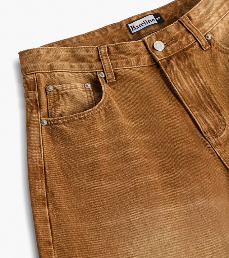 Detail flat lay photography of a tan denim waistband with button and stitching