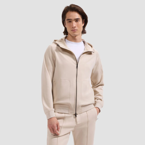 Model in cream zip-up hoodie and matching sweatpants, hands in pockets, front view