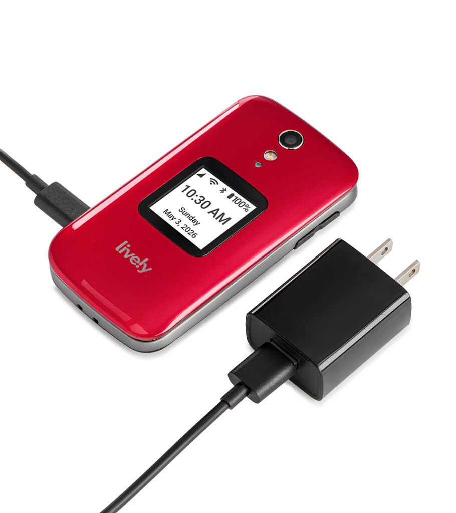 Product photography of a red clamshell flip phone with its screen lit, shown alongside a black wall charger and cable