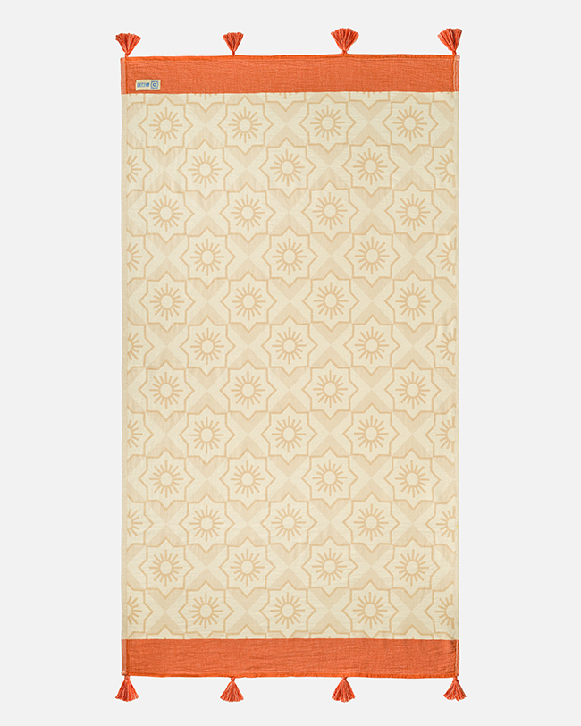 Product photography of a cream cotton towel with a tonal medallion pattern and terracotta border, laid flat