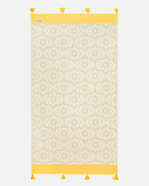 Flat lay photography of a cream towel with a tonal sun-medallion weave and yellow tasselled border, shown full length