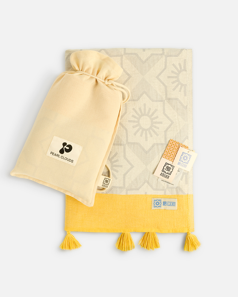 Product photography of a cream drawstring pouch shown with a folded yellow tasselled towel