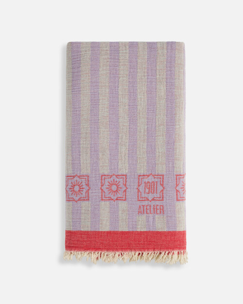 Product photography of a folded lavender and grey striped towel with a red border band and fringed edge