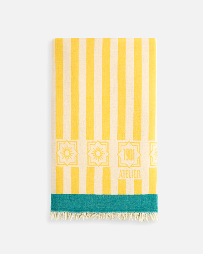 Product photography of a folded yellow and white striped towel with a teal band and fringe