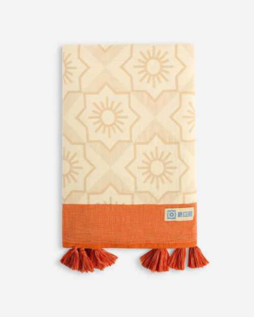 Product photography of a folded cream towel with a floral medallion weave and a terracotta band with tassels