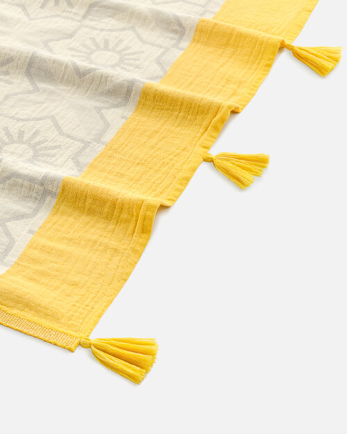 Close-up product photography of the tasselled corner of a cream medallion-weave towel with a yellow band