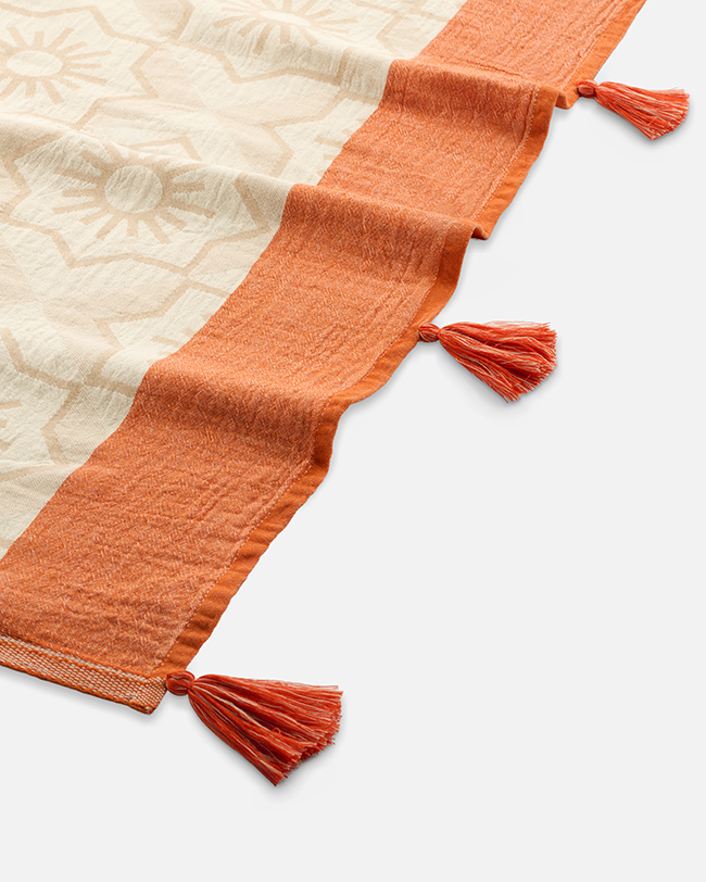 Close-up product photography of the terracotta tasselled border on a cream patterned towel