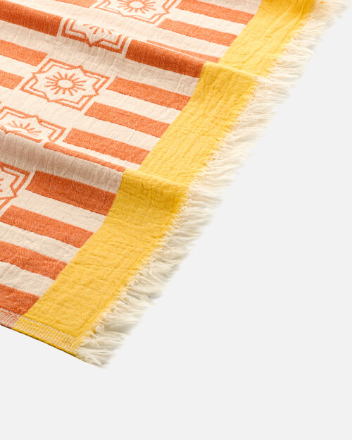 Close-up product photography of the fringed corner of an orange striped towel with a yellow band