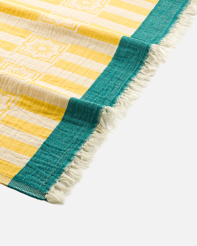 Close-up product photography of the fringed corner of a yellow striped towel with a teal band