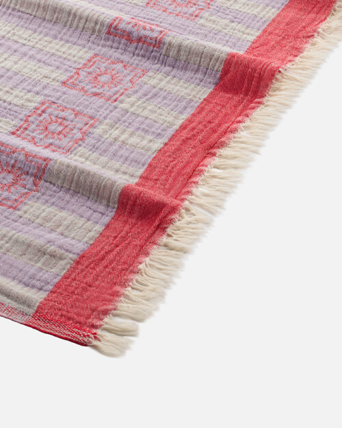 Close-up product photography of the fringed corner of a lavender striped towel with a red band