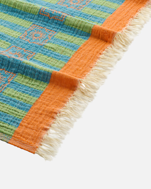 Close-up product photography of the fringed corner of a green and blue striped towel with an orange band