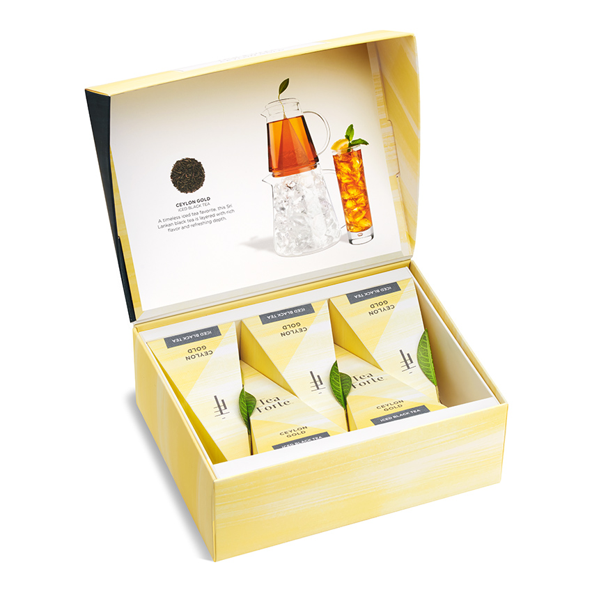 Product photography of an open yellow gift box of pyramid tea sachets with a printed insert showing a citrus iced tea serve