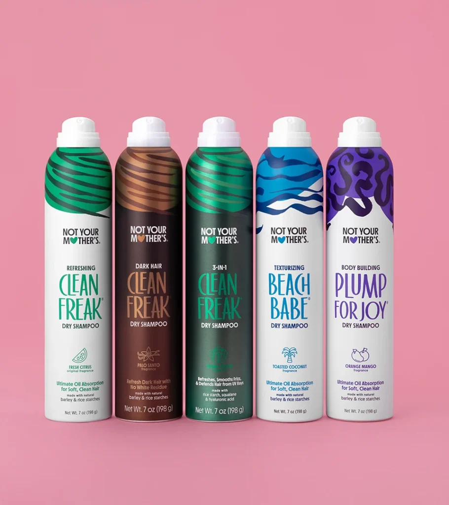 Grouped product photography of five haircare mousse cans in green, brown, blue and purple label designs, lined up on a pink background