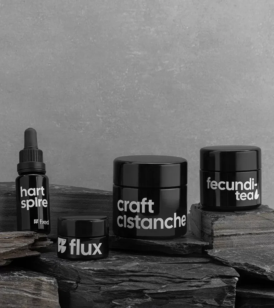 Editorial product photography of a dropper bottle and three black jars styled on stone against a grey sky