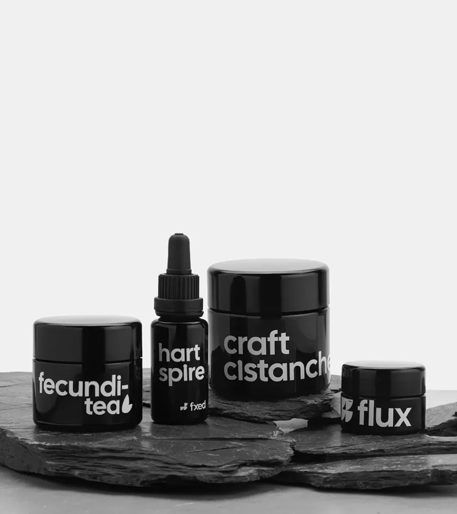 Editorial product photography of a black dropper bottle with four black supplement jars arranged on a dark stone surface