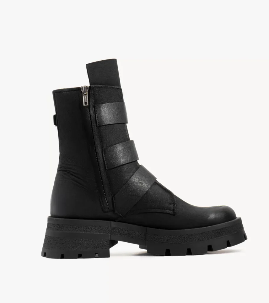 Shoe product photography of a black leather zip-front boot in side profile with strap detail on a chunky lugged sole