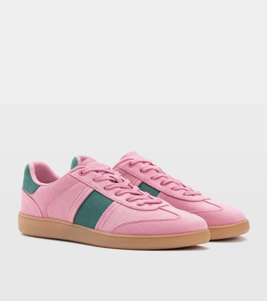 Shoe product photography of a pink suede retro trainer at a front three-quarter angle with a green side stripe and gum sole
