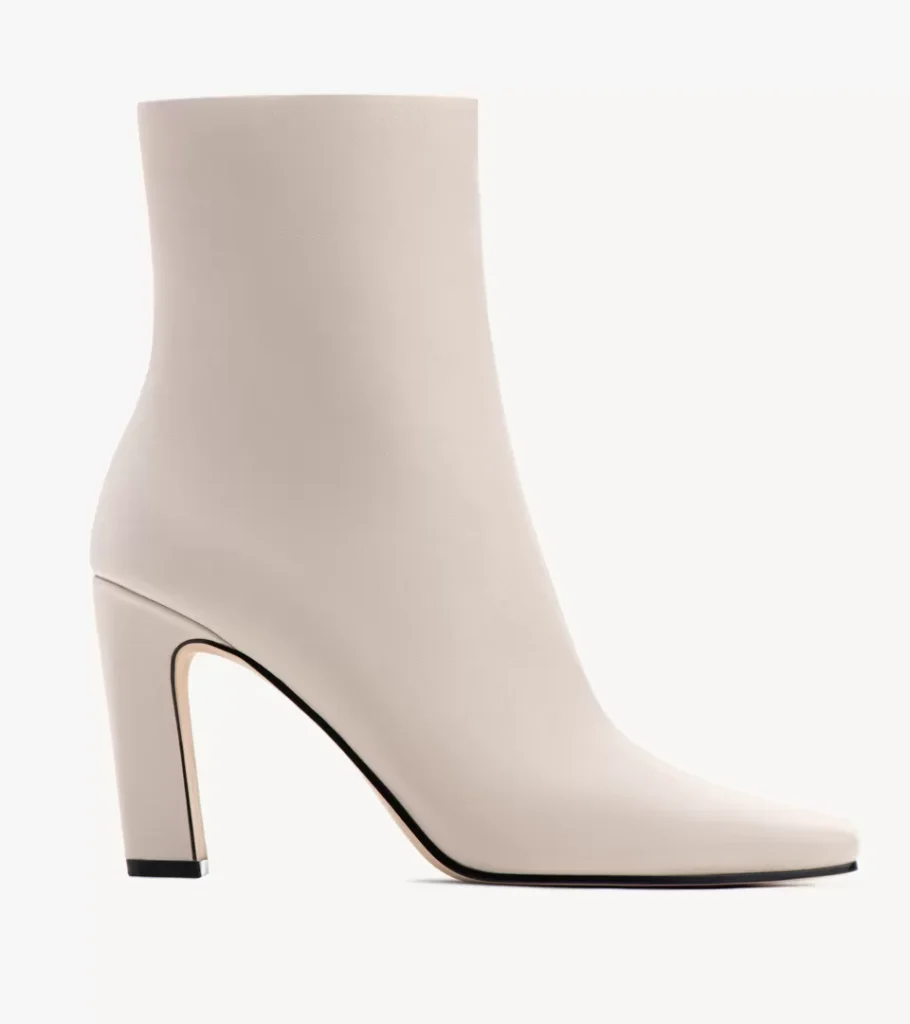 Shoe product photography of a cream leather ankle boot in side profile with a pointed toe and high block heel