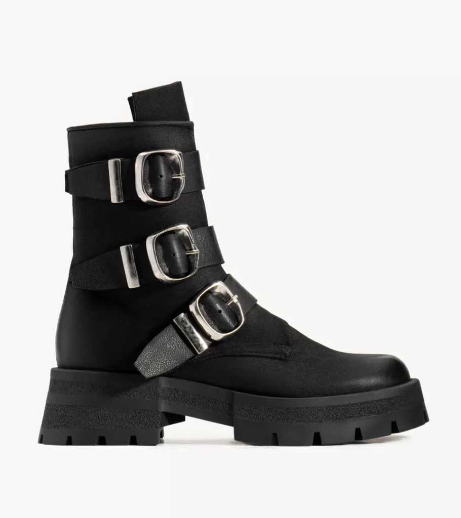 Shoe product photography of a black leather combat boot in side profile with three silver buckle straps on a lugged sole