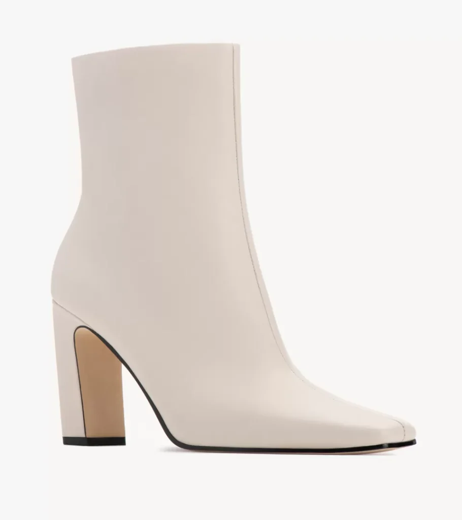 Shoe product photography of a cream leather ankle boot at a front three-quarter angle showing the pointed toe and block heel