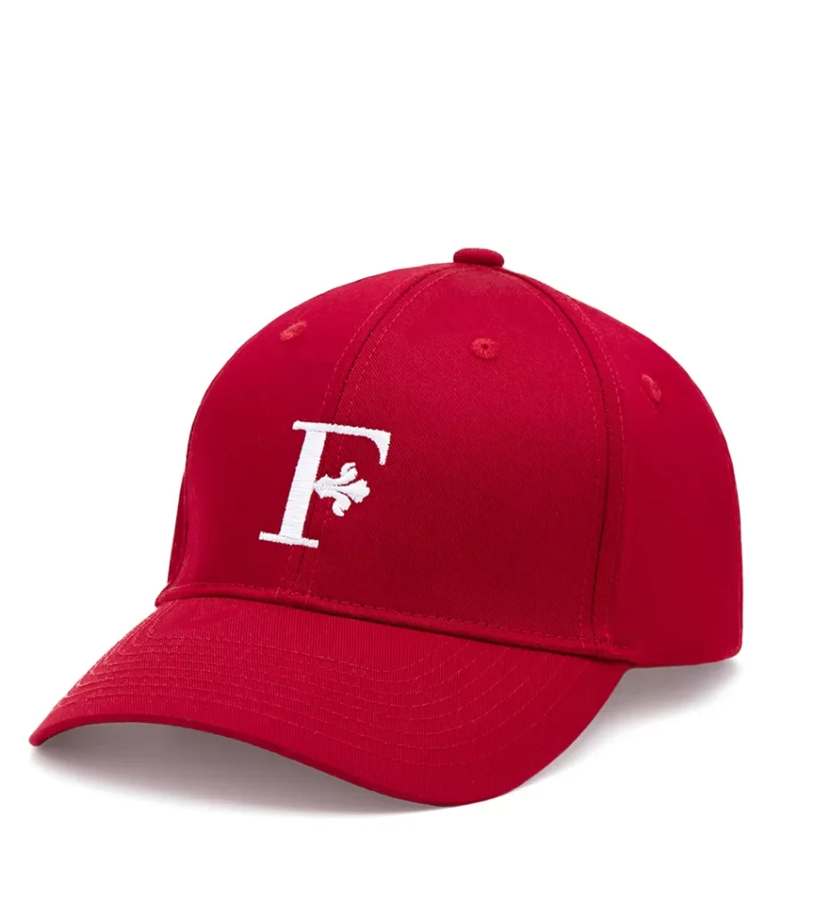 Product photography of a red baseball cap with a white embroidered letter monogram, side view