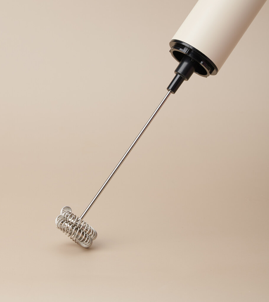 Close-up product photography of the coiled stainless steel whisk head on a cream handheld frother