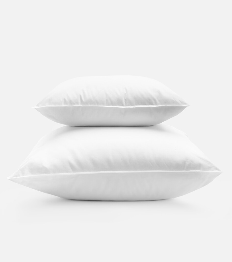 Product photography of two white bed pillows stacked one above the other, on white