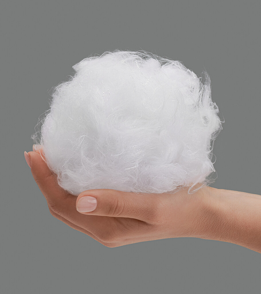 Close-up product photography of a hand holding a cluster of white fibre filling, on grey