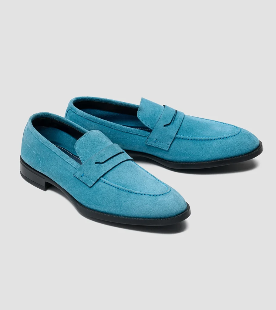 Shoe product photography of a pair of turquoise suede penny loafers at a front three-quarter angle