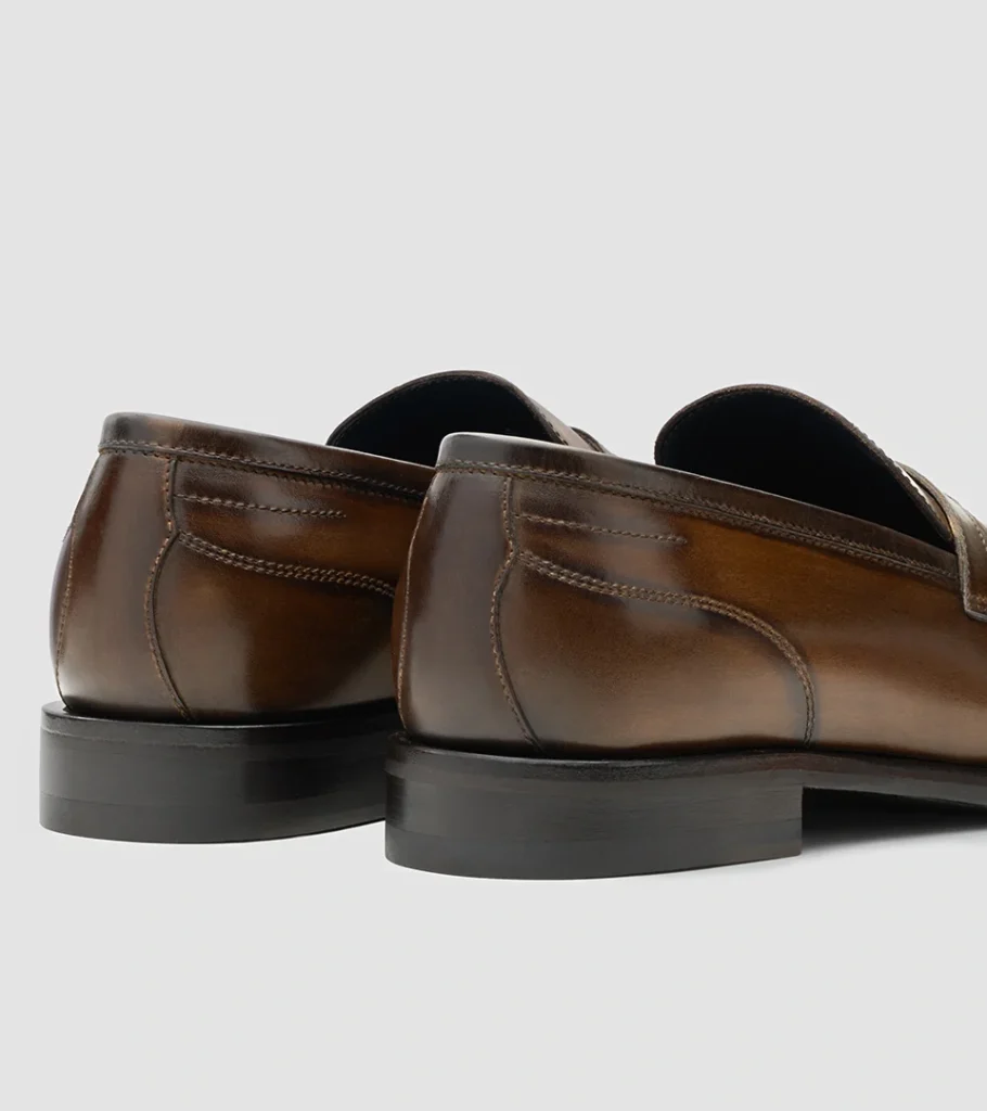 Shoe product photography of a pair of burnished brown loafers viewed from behind showing heel counters and sole edges