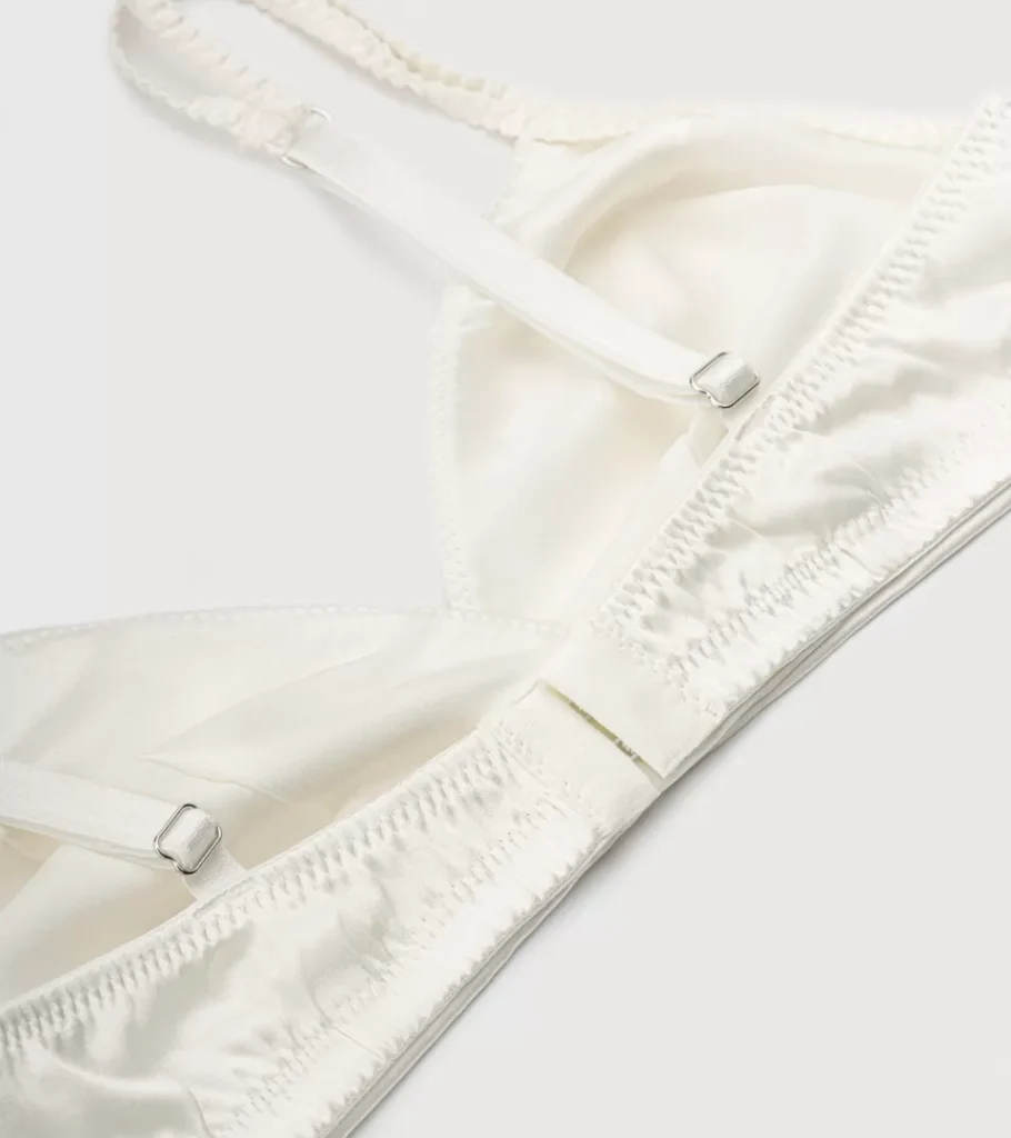 Close-up product photography of the strap slider and stitching detail on an ivory satin bra