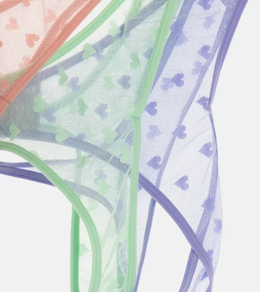 Flat lay photography of three sheer briefs in coral, green and lilac with a printed heart pattern, layered together