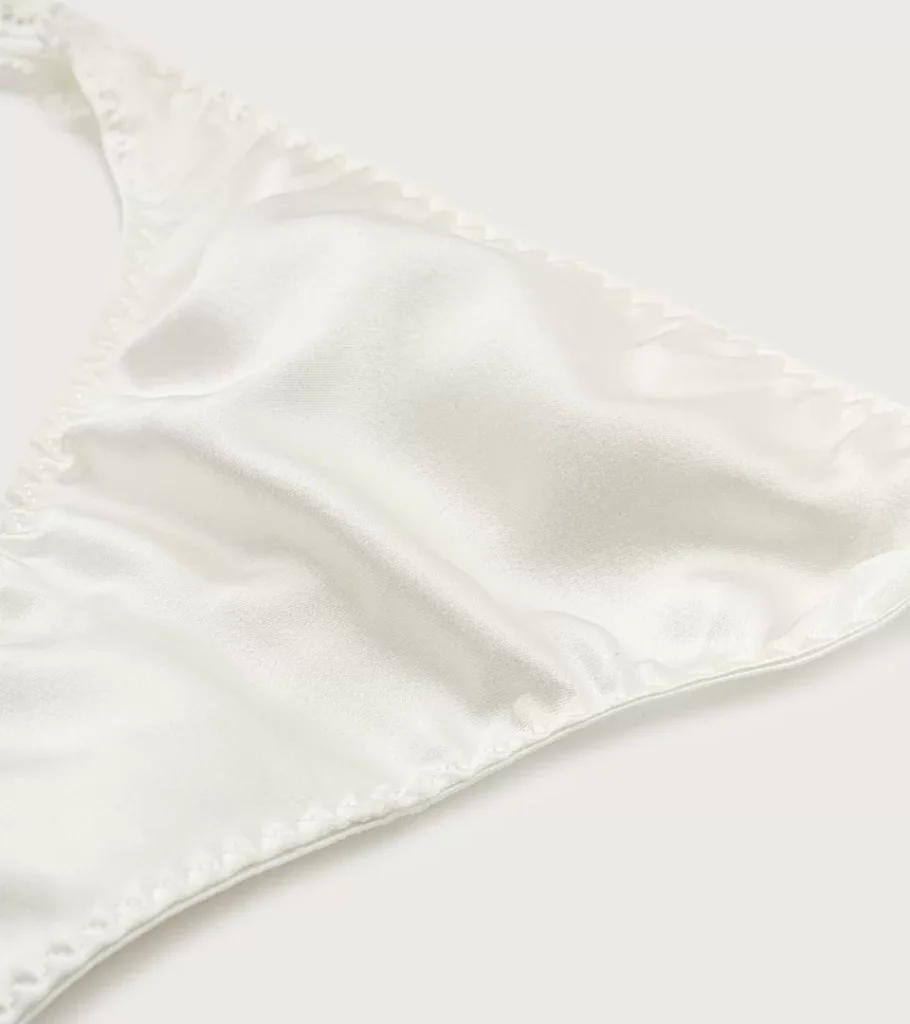 Flat lay photography of an ivory satin bralette with adjustable straps, shown on a light background