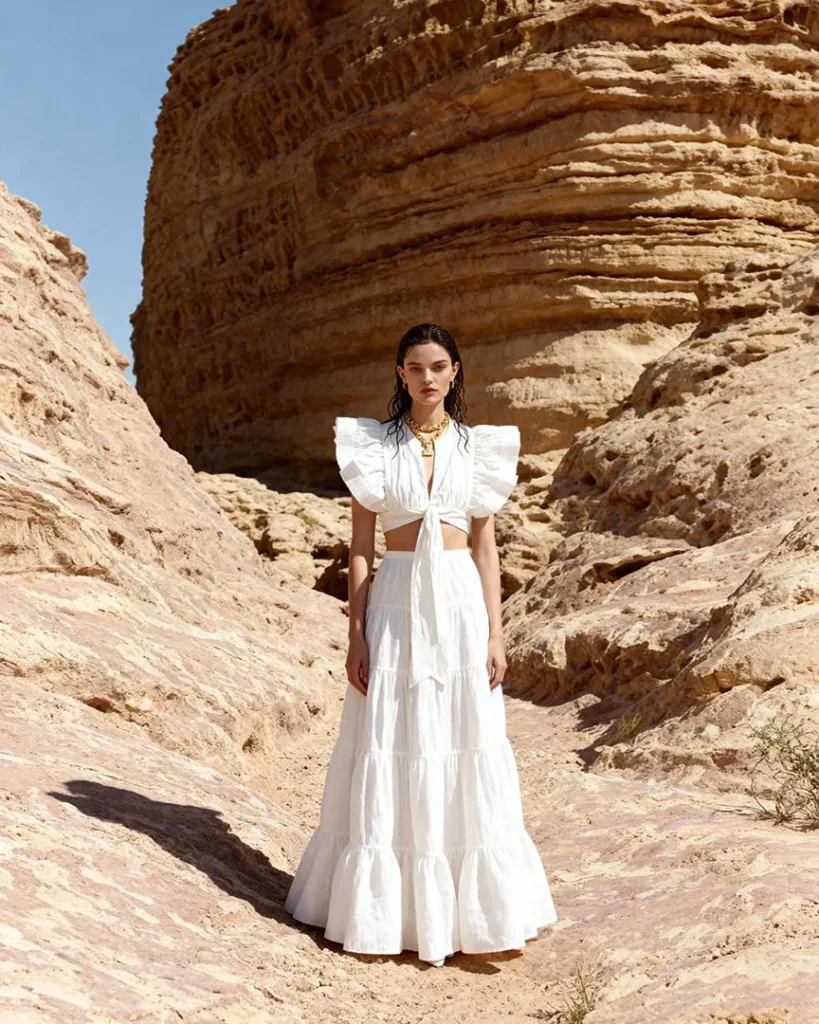 AI model photography of a white tiered maxi skirt with a ruffled-sleeve tie-front top, editorial scene in a sandstone canyon