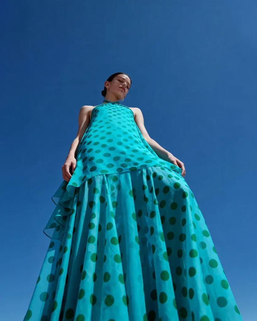 AI model photography of a turquoise organza gown with green polka dots, low-angle editorial view against a deep blue sky